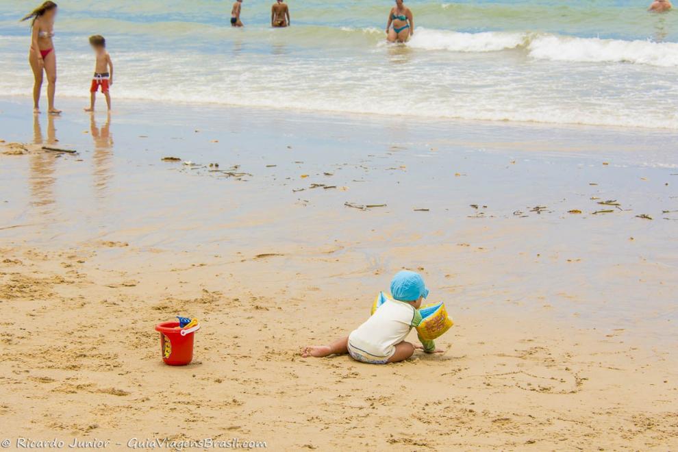 Imagem de um menino com boinhas brincando nas areias na beira do mar.